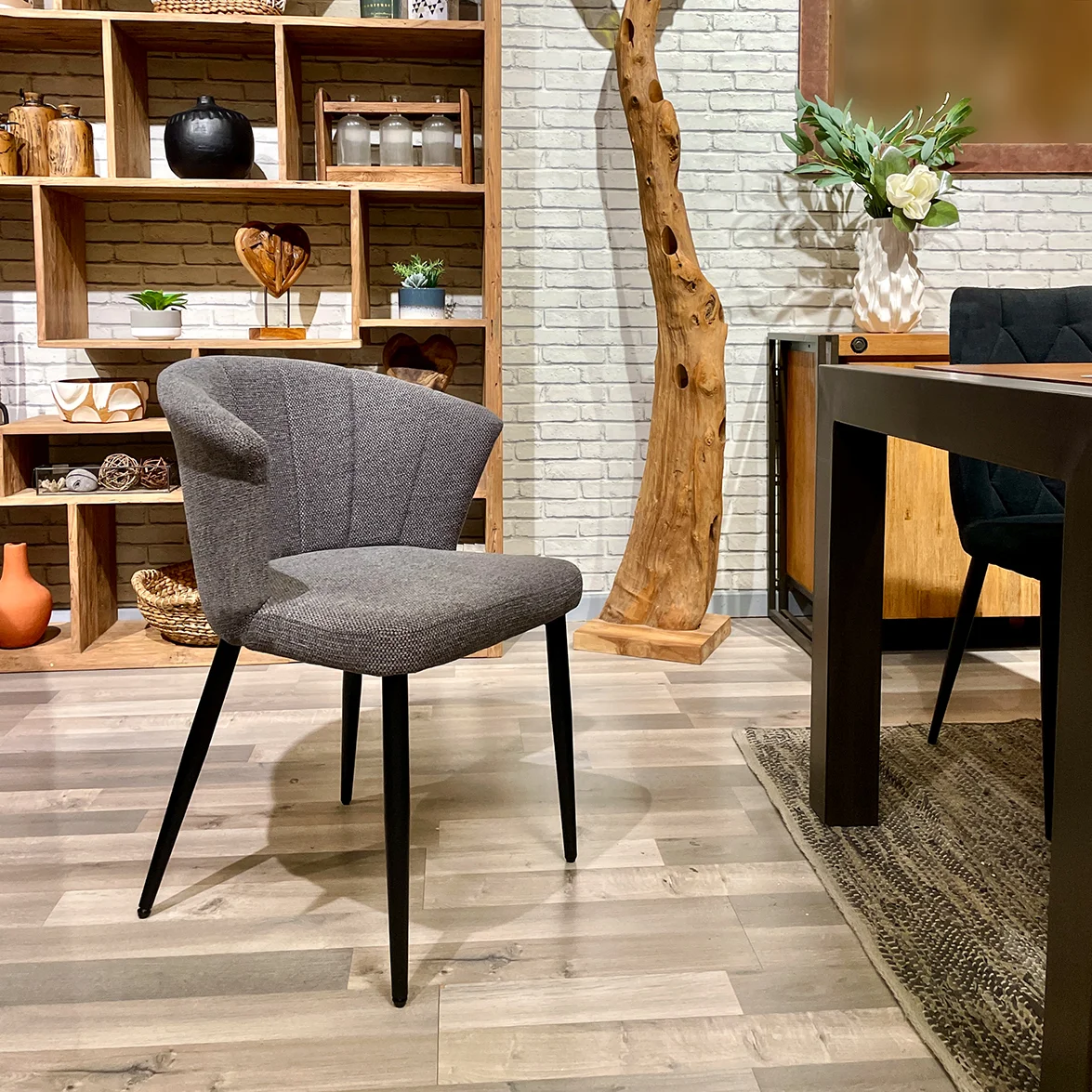 Photo d'ambiance d'une chaise de repas de en tissu gris, placée au sein d'une salle à manger à la décoration chaleureuse.