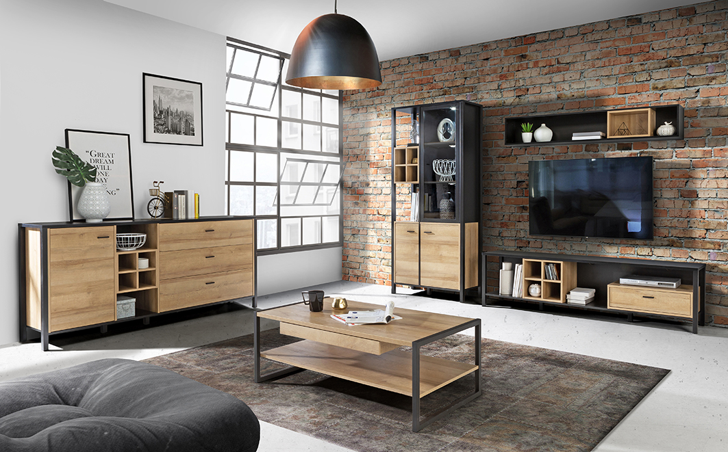 Un salon à l'ambiance loft, avec de grandes fenêtre style atelier et un mur en briques, faisant ressortir les meubles de la collection MODE qui associent décor de bois et structure en métal noir. 