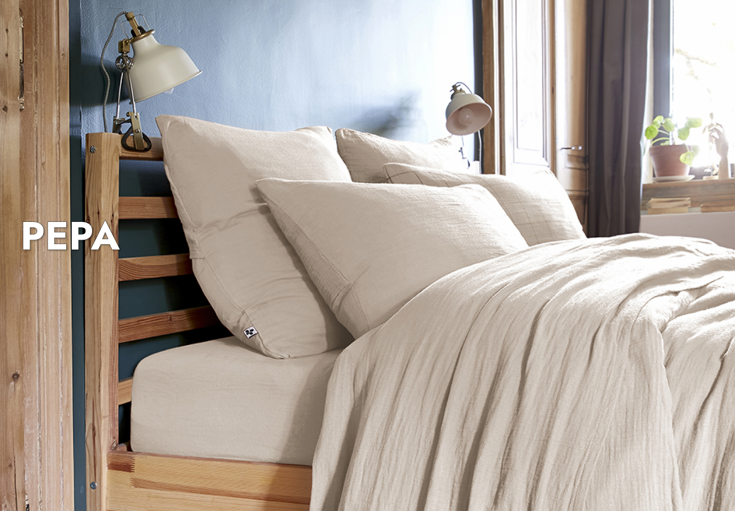 Un lit en bois clair dans une chambre à coucher à la décoration bohème. Sur le lit, les draps en gaze de coton de la collection PEPA, couleur blanc. Sont présents : les taies d'oreiller 50 x 50 et 50 x70, la housse de couette, le drap housse et le drap plat.  